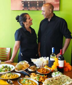 Chef Sunil Kumar and Pushpa Kumar standing behind a table of Marigold Maison dishes, naan and marigold flowers