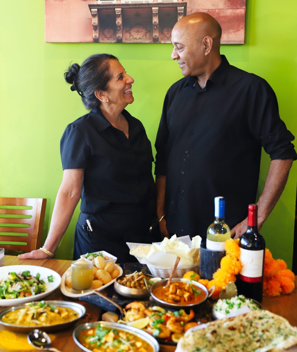 Chef Sunil Kumar and Pushpa Kumar standing behind a table of Marigold Maison dishes, naan and marigold flowers